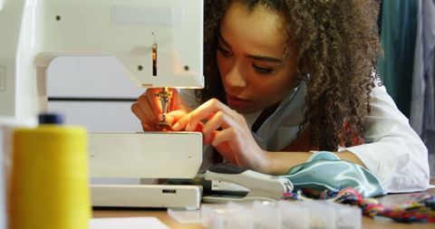 Focused fashion designer threading sewing machine in workshop