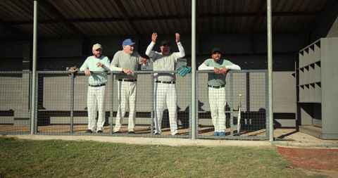 Baseball teammates cheering from dugout behind chainlink fence on sunny grass field