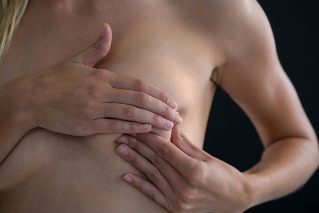 Woman checking lumps while checking breast against black background