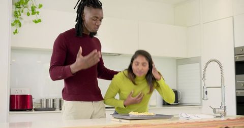 Diverse couple baking together on kitchen island sharing laugh after pastry mishap