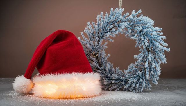 Red Velvet Santa Hat with Glowing Faux-Fur Brim and Frosted Wreath on Tabletop