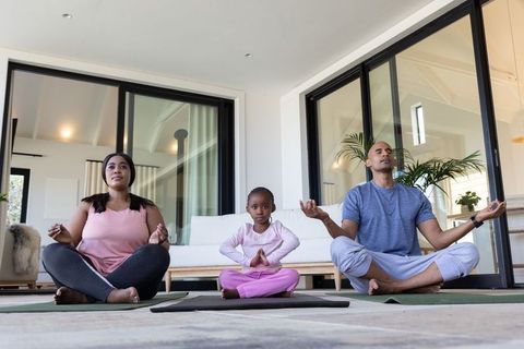 African american family practicing mindful yoga at home, parents and child meditating