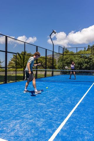 Diverse players rallying on bright blue padel court under sunny sky with floodlight
