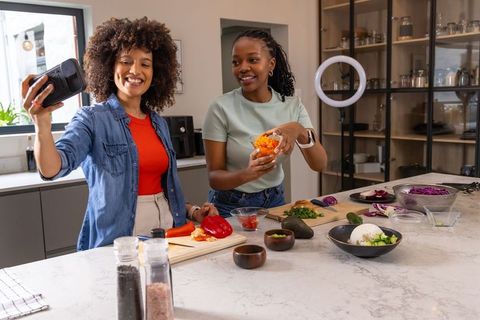 African American women recording cooking video at kitchen island with ring light