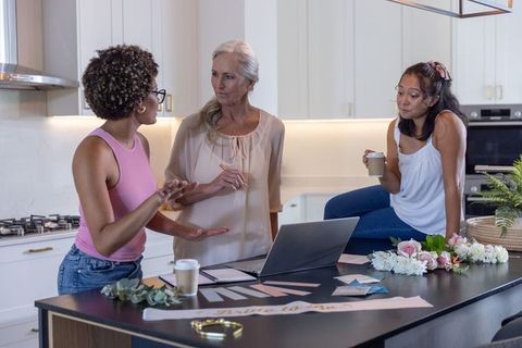 Diverse women planning bridal table decor at modern kitchen island with laptop and coffee