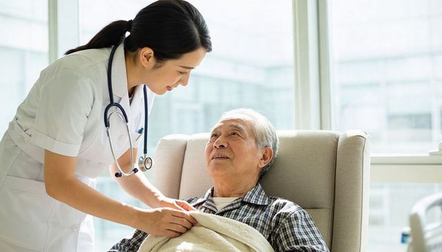 Nurse tucking blanket for senior in bright medical recliner, compassionate elder care