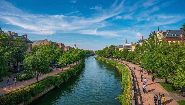 Flowing central canal with tree-lined promenades, historic buildings, urban riverside walkway and ch