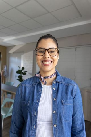 Smiling asian woman wearing glasses and scarf in modern open-plan living space