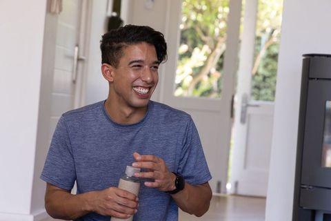Sunlit african american man smiling while holding reusable water bottle in entryway