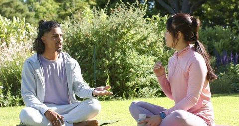 African american couple talking and relaxing on yoga mats in sunny park garden