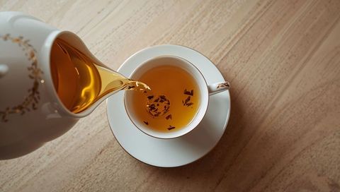 Pouring golden tea from porcelain teapot into white cup overhead minimal flatlay