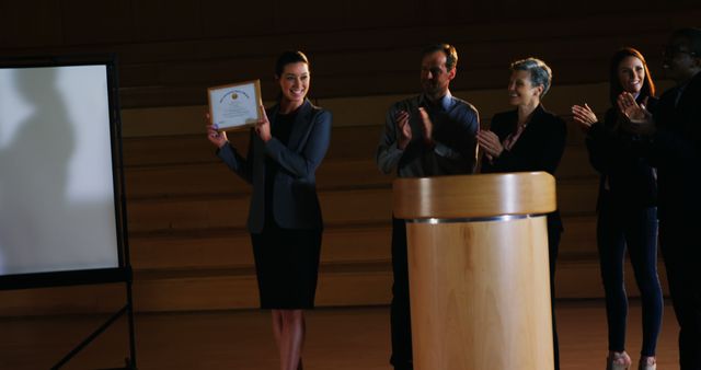 A young Caucasian woman is receiving an award in a professional setting, with copy space. Colleagues are applauding her achievement, highlighting a moment of recognition and success within a business or academic environment.
