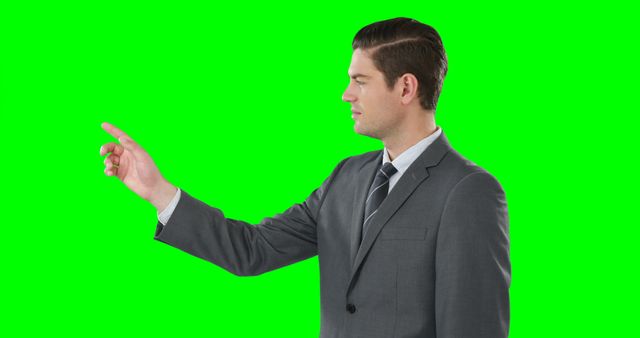 A Caucasian businessman in a gray suit is gesturing with his finger to an invisible point, with copy space on a green screen background. His pose suggests he's presenting or interacting with a digital interface or virtual element.