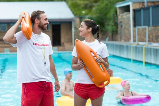 Male and female lifeguards holding rescue cans at poolside