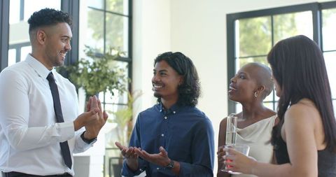 Diverse colleagues networking and chatting in modern office reception holding drinks