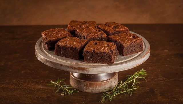 Serving rich fudgy chocolate brownies on rustic metal cake stand with rosemary