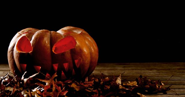 A carved pumpkin with a menacing face glows ominously in the dark, surrounded by fallen autumn leaves, with copy space. Its glowing eyes and sharp teeth create a spooky atmosphere, typical of Halloween celebrations.