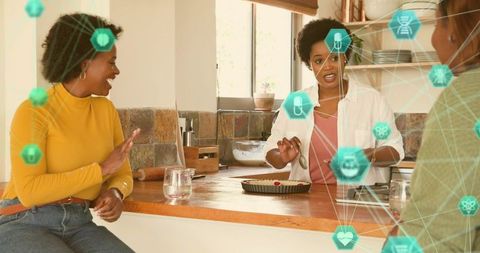 Laughing friends baking tart in cozy kitchen with digital health food icons network