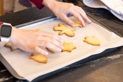 Hands arranging baked gingerbread cookies on parchment-lined tray wearing smartwatch cozy kitchen