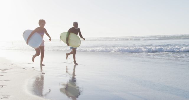 Couple running on the beach carrying surfboards during sunset. Perfect for advertising beach vacations, surf schools, outdoor activities, and healthy lifestyle promos.