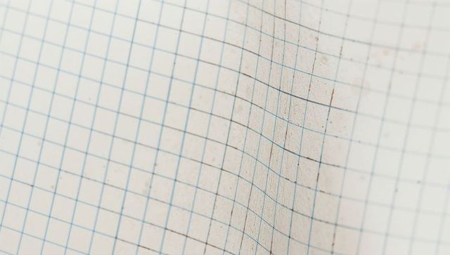 Curving squared graph paper closeup showing blue grid, smudges and crease texture