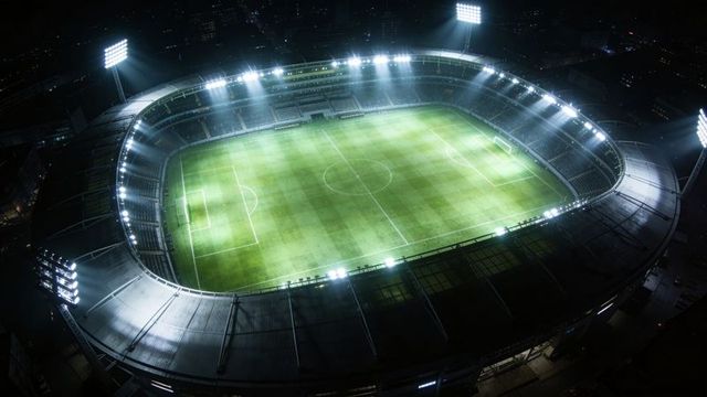 Aerial nighttime football stadium floodlit arena over urban landscape for sports events