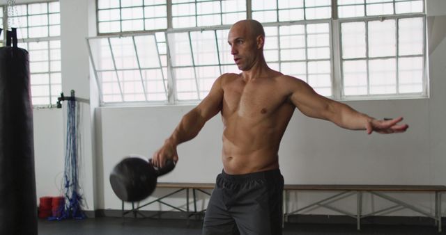 Muscular man lifting kettlebell in gym, showcasing strength and fitness. Ideal for fitness websites, gym promotions, workout tutorials, and health magazines.
