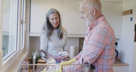 Middle-aged couple washing dishes together in cozy kitchen