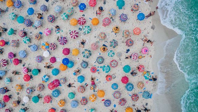 Aerial view showing colorful beach umbrellas dotting sandy shore beside turquoise sea