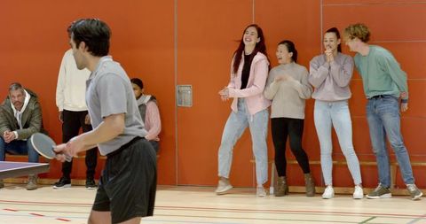 Diverse friends cheering table tennis in sports hall