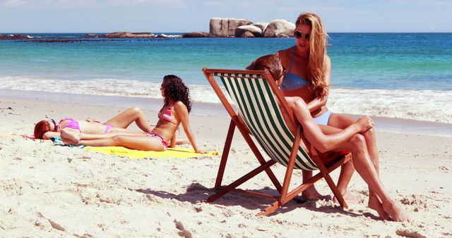 Group of friends enjoying sunny day on sandy beach with clear blue ocean in the background. People lounging and sunbathing, taking a break from their activities to relax. Perfect for topics related to summer vacations, relaxation, seaside holidays, and beachside leisure.