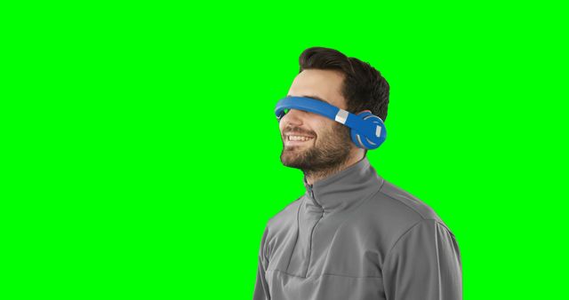 Young man using virtual reality headset enjoying an immersive experience while smiling. The green screen background allows for easy customization or replacement in multimedia projects. Suitable for tech revviews, VR experiences, promotional materials, and advertisements highlighting innovative technology and user engagement.