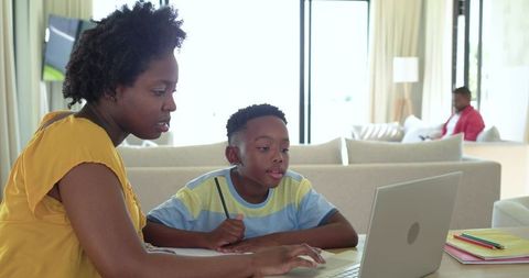 African american mother helping son with laptop homework in bright modern living room