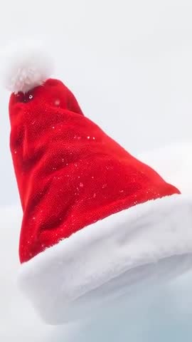Rotating Santa hat drifting over snowy field with gentle flurry vertical holiday loop