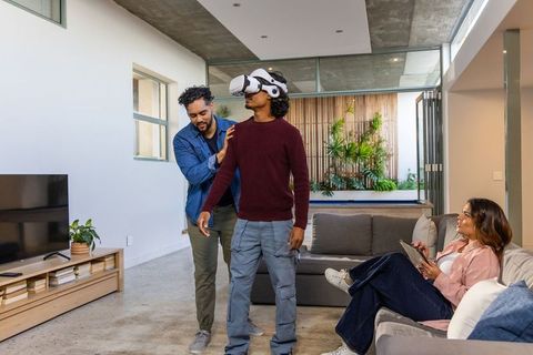 Friends guiding indian man experiencing virtual reality headset in modern living room