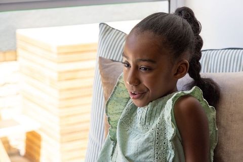 African american girl relaxing on sofa by window in green ruffled dress