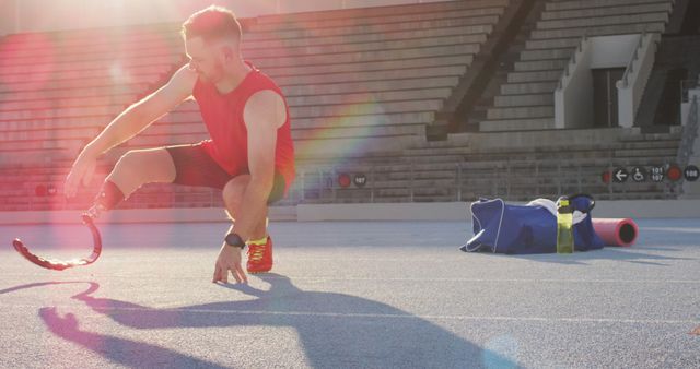 Paralympic athlete wearing prosthetic leg stretching on racetrack during sunrise, preparing for workout. Perfect for showcasing athletic determination, advertising sportswear, or inspirational content about overcoming challenges and triumph in sports.