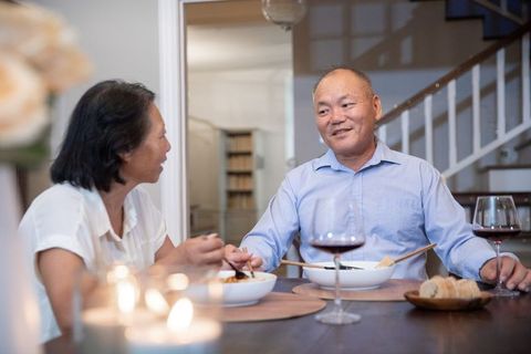 Asian couple enjoying candlelit dinner at home sharing wine, chopsticks and cozy ambience