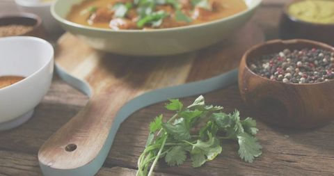 Fresh cilantro bunch resting on rustic wooden board with peppercorns and bowls