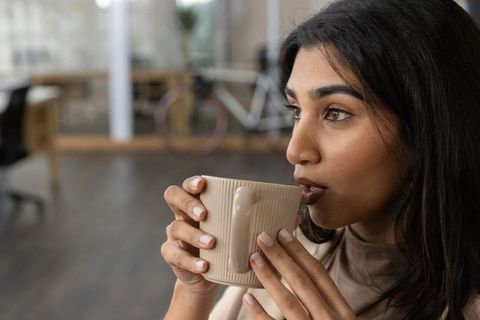 Indian professional sipping coffee from ribbed ceramic mug in modern coworking office