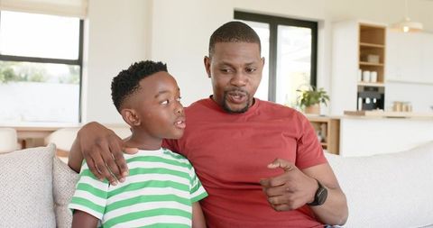 African american father bonding with son on sunlit couch pointing and talking