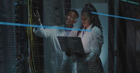 It technicians diagnosing server rack using laptop and patch cables in blue-lit data center