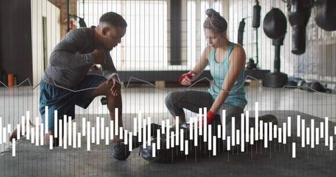 Kneeling coach guiding athlete adjusting kettlebell and sandbag with red hand wraps for boxing