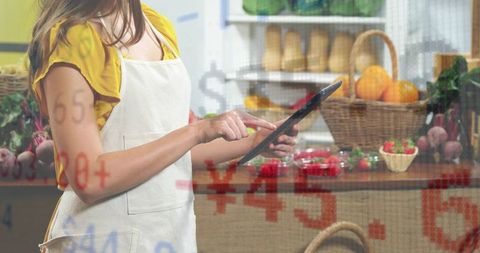 Vendor checking prices on tablet at farmers market, fresh produce, baskets and display