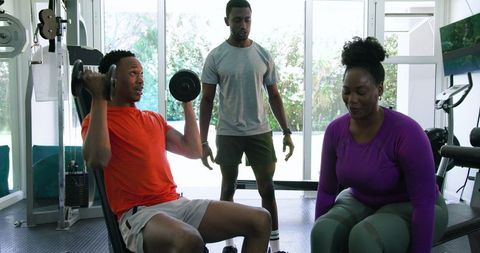 Couple Exercising with Dumbbells Under Trainer's Guidance at Home Gym