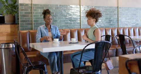 Two african american women having coffee and talking at cafe banquette, casual conversation