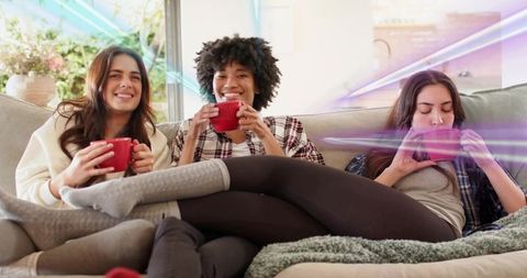 Three friends relaxing on sofa with red mugs in cozy loungewear and casual home interior