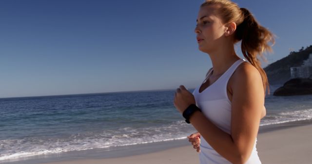 A young Caucasian woman jogs along a serene beach during the day, with copy space. Her focus and active lifestyle are emphasized against the tranquil backdrop of the ocean.