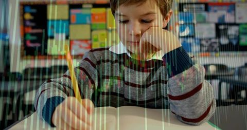 Elementary student writing at school desk holding pencil concentrating on notebook and learning