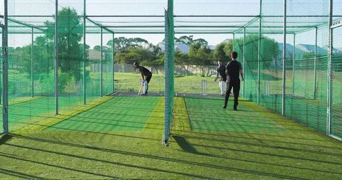 Practicing cricket batsmen in outdoor net lanes on artificial turf during training